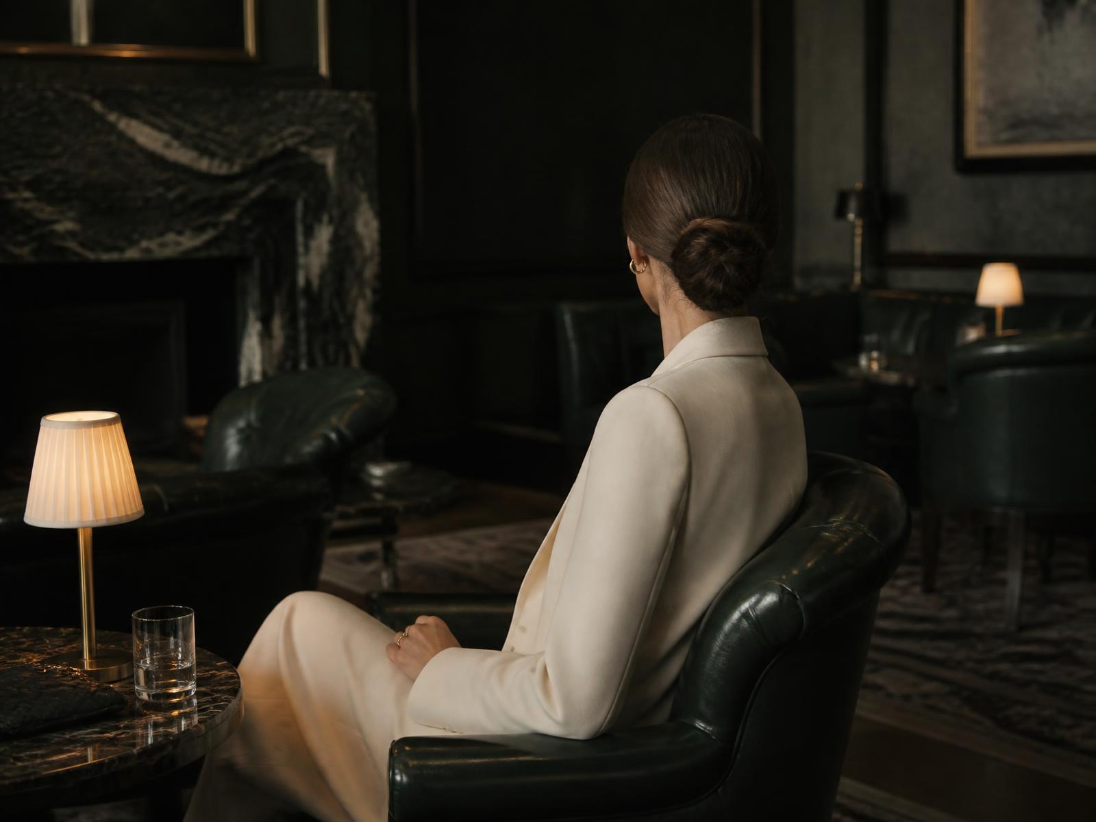 A quiet private club interior at dusk, low lamplight on dark wood and velvet